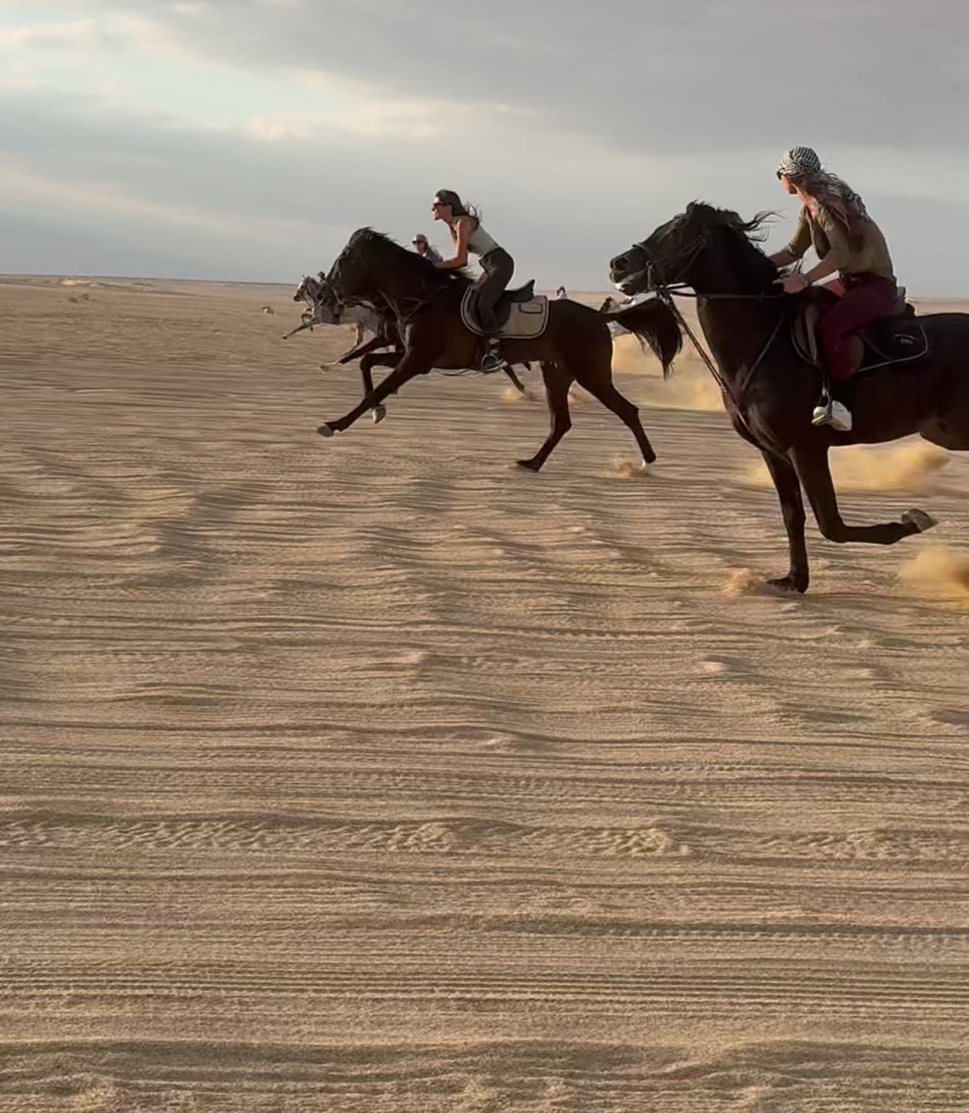 Jinetes galopando por el desierto al atardecer